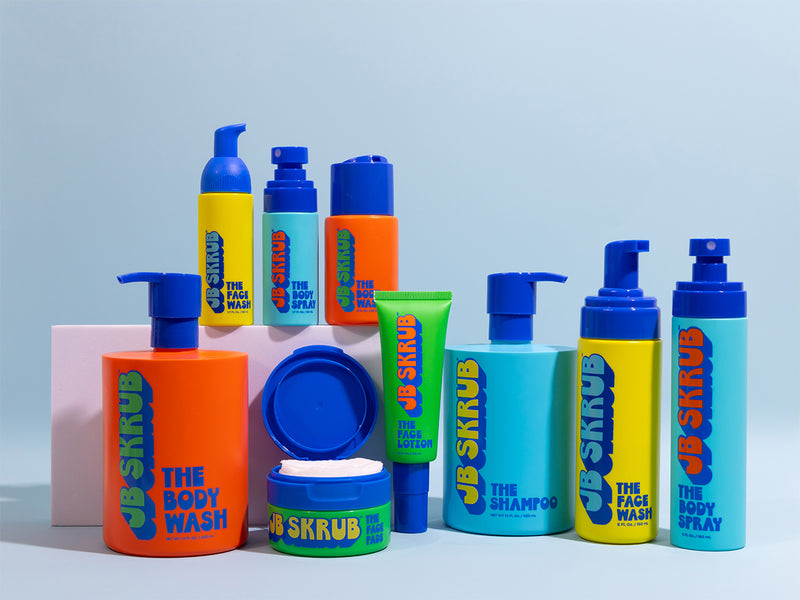 Collection of colorful skincare products with 'JB Skrub' branding on a light blue background